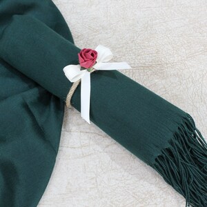 May include: A dark green scarf with a white ribbon and a small red flower tied around it.