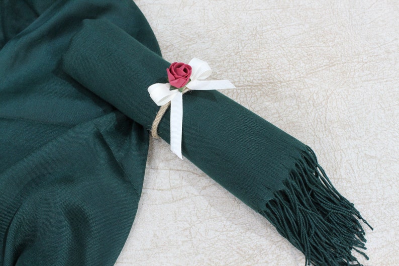 May include: A dark green scarf with a white ribbon and a small red flower tied around it.