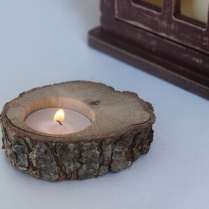 May include: A wooden candle holder made from a tree slice with a small white candle burning inside.