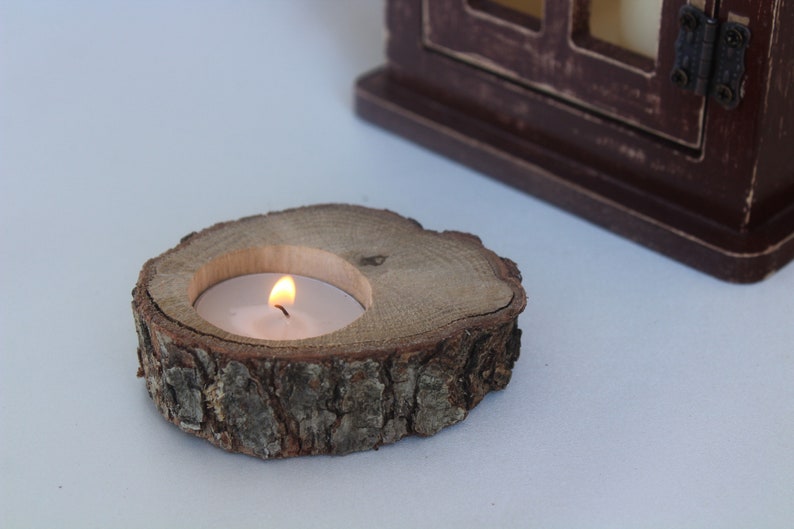 May include: A wooden candle holder made from a tree slice with a small white candle burning inside.
