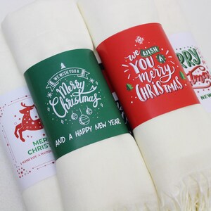 Pode incluir: Quatro sacos de presente de tecido branco com etiquetas de presente de papel com tema natalino. As etiquetas s&atilde;o de cor vermelha, verde e branca com texto escrito &agrave; m&atilde;o que diz "We wish you a Merry Christmas and a Happy New Year", "We wish you a Merry Christmas", "Merry Christmas", e "We wish you a Merry Christmas".
