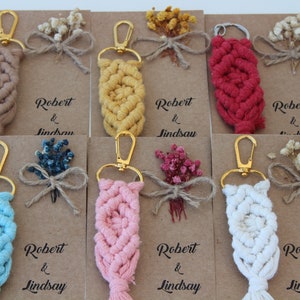 Puede incluir: Conjunto de diez llaveros con un dise&ntilde;o de macram&eacute; en varios colores, incluyendo beige, amarillo, rojo, azul, rosa y blanco. Cada llavero tiene un cierre de metal dorado y est&aacute; unido a una peque&ntilde;a tarjeta con el texto "Robert & Lindsay" impreso en ella. Las tarjetas est&aacute;n decoradas con flores secas.