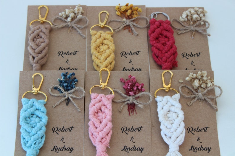 Puede incluir: Conjunto de diez llaveros con un dise&ntilde;o de macram&eacute; en varios colores, incluyendo beige, amarillo, rojo, azul, rosa y blanco. Cada llavero tiene un cierre de metal dorado y est&aacute; unido a una peque&ntilde;a tarjeta con el texto "Robert & Lindsay" impreso en ella. Las tarjetas est&aacute;n decoradas con flores secas.
