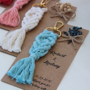 Puede incluir: Un conjunto de cuatro llaveros con un dise&ntilde;o de macram&eacute; y un borla. Cada llavero est&aacute; en una tarjeta marr&oacute;n con el texto "Robert & Lindsay 10.23.2020 Gracias por celebrar con nosotros".