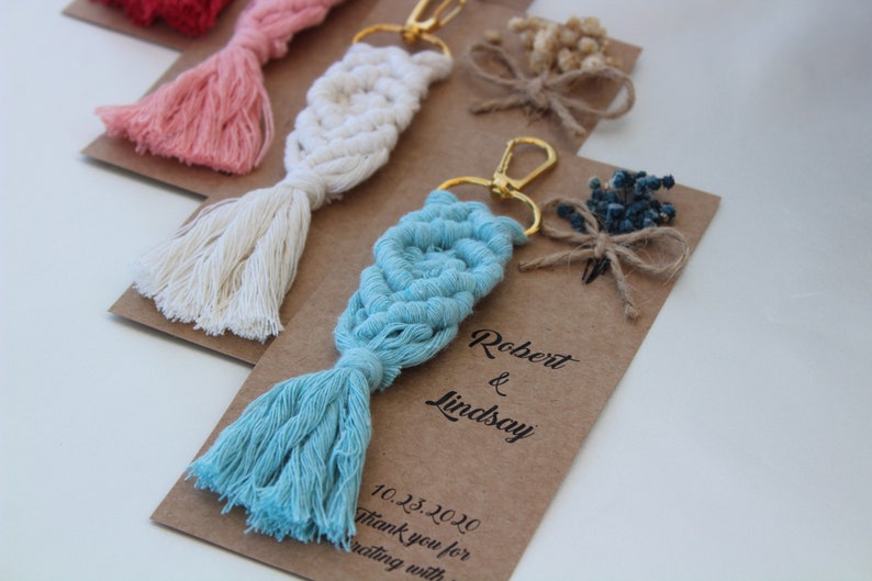 Puede incluir: Un conjunto de cuatro llaveros con un dise&ntilde;o de macram&eacute; y un borla. Cada llavero est&aacute; en una tarjeta marr&oacute;n con el texto "Robert & Lindsay 10.23.2020 Gracias por celebrar con nosotros".
