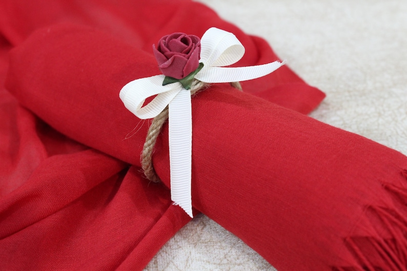 May include: A red scarf with a white ribbon and a red rose tied around it.
