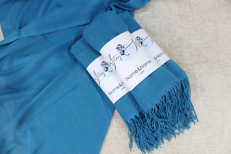 May include: Three teal blue pashmina scarves with fringed edges. Each scarf has a white label with the text "Stay" and "Name & Name" with a space for a date.