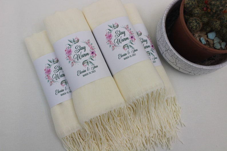 May include: Four ivory white pashmina scarves with floral designs and the text "Stay Warm" and "Elenia & Jan" with the date "March 19, 2022".