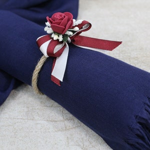 May include: A navy blue scarf with a fringe trim is tied with a red and white ribbon and a red rose.