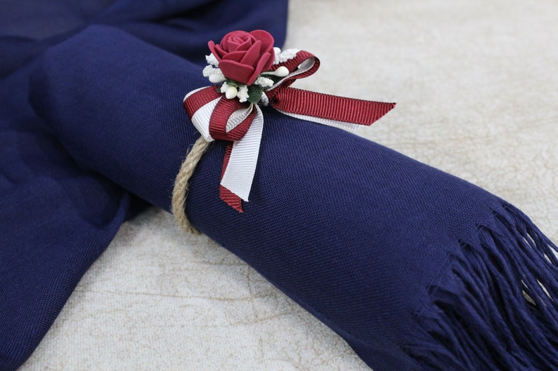 May include: A navy blue scarf with a fringe trim is tied with a red and white ribbon and a red rose.
