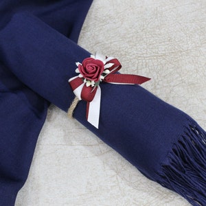 May include: A navy blue pashmina scarf with a burgundy and white ribbon tied around it. A burgundy rose with white accents is attached to the ribbon.