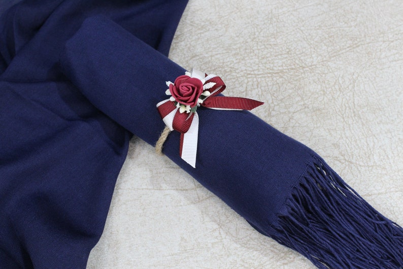 May include: A navy blue pashmina scarf with a burgundy and white ribbon tied around it. A burgundy rose with white accents is attached to the ribbon.
