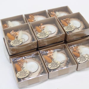 K&ouml;nnte beinhalten: Neun kleine Geschenkboxen mit transparenten Deckeln. Jede Box enth&auml;lt eine Holzscheibe mit einer wei&szlig;en Kerze, Trockenblumen und einem Etikett mit der Aufschrift "Thank You For Showering our Little Pumpkin..." f&uuml;r eine Babyparty.