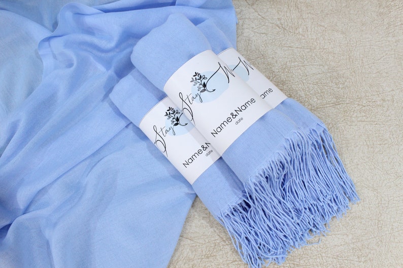 Pu&ograve; includere: Due sciarpe di pashmina blu chiaro con frange, avvolte e legate insieme con un'etichetta bianca che dice "Stay & Name & Name & date".