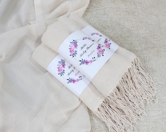 Könnte beinhalten: Zwei weiße Pashmina-Schals mit Blumendesigns und dem Text "Hello Baby Shower" und "Kristen" auf den Etiketten.