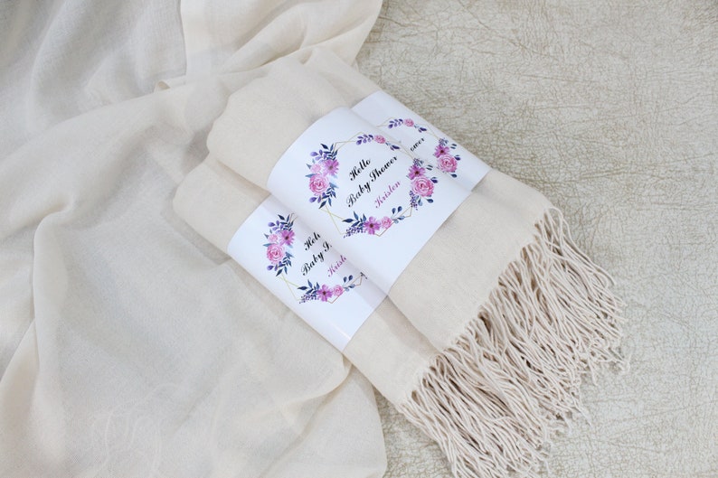 May include: Two white pashmina scarves with floral designs and the text "Hello Baby Shower" and "Kristen" on the labels.