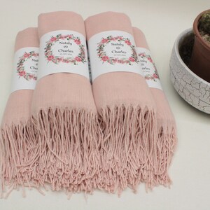 May include: Four pink pashmina scarves with fringe edges. Each scarf has a white label with a floral design and the text "Nataly & Charles" on it.