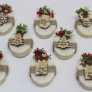 May include: Oval-shaped soaps decorated with dried flowers and wooden ornaments. Each soap is wrapped with twine and features a different holiday design, including a snowflake, Christmas tree, and reindeer, with the text "Merry Christmas 2024" and "Happy New Year 2024".