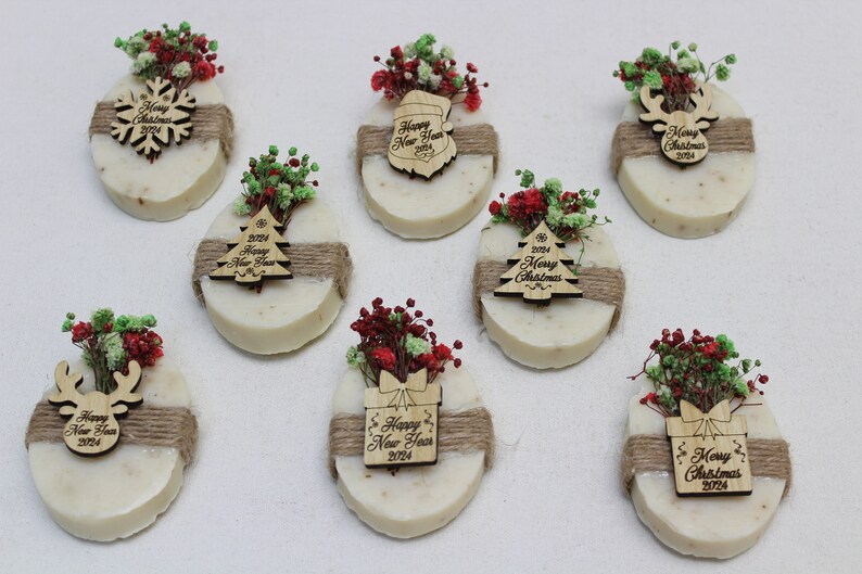 May include: Oval-shaped soaps decorated with dried flowers and wooden ornaments. Each soap is wrapped with twine and features a different holiday design, including a snowflake, Christmas tree, and reindeer, with the text "Merry Christmas 2024" and "Happy New Year 2024".