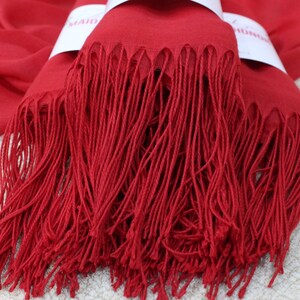 May include: A red pashmina scarf with long fringe. The scarf is folded in half and the fringe is visible on both sides.