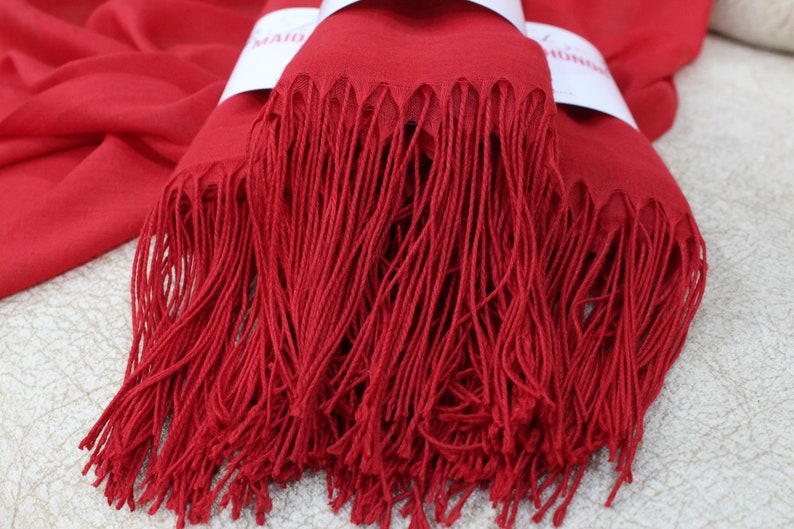 May include: A red pashmina scarf with long fringe. The scarf is folded in half and the fringe is visible on both sides.