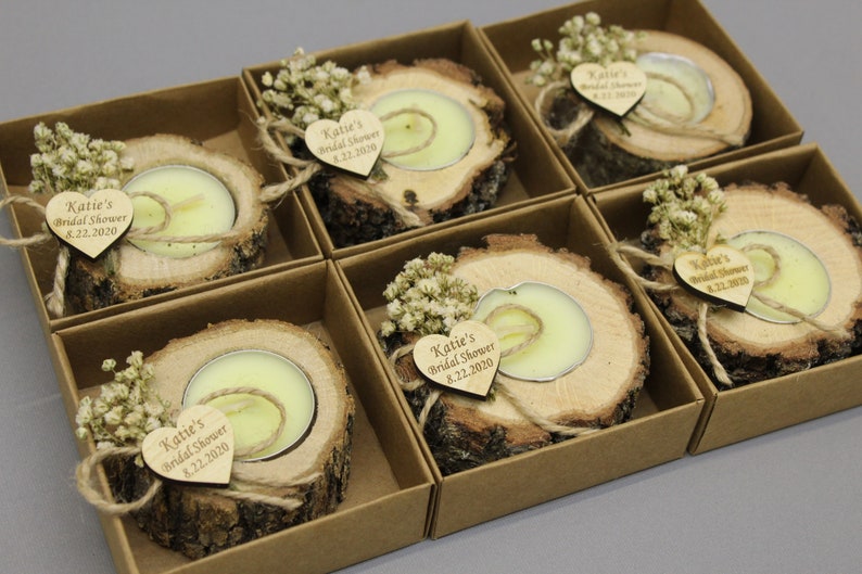Op de afbeelding: Set van zes rustieke houten kaarsenhouders met kleine witte bloemen en een hartvormig label met de tekst "Katie's Bridal Shower 8.22.2020".