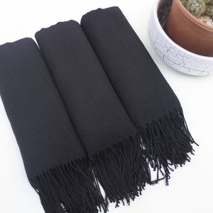 May include: Three black scarves with fringe. The scarves are folded and stacked on top of each other.