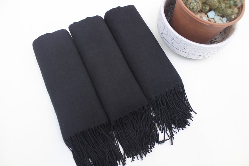May include: Three black scarves with fringe. The scarves are folded and stacked on top of each other.