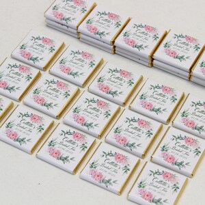 Puede incluir: Una colecci&oacute;n de peque&ntilde;as barras de chocolate blanco con envoltorios de papel de aluminio dorado. Cada barra presenta un dise&ntilde;o floral con flores rosas y hojas verdes. El texto "Collette's Bridal Tea" est&aacute; impreso en cada barra.