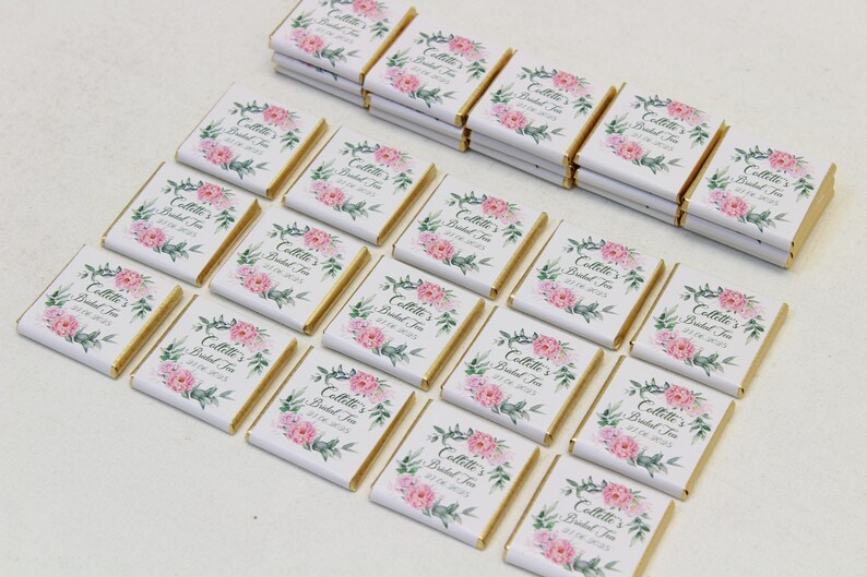 Puede incluir: Una colecci&oacute;n de peque&ntilde;as barras de chocolate blanco con envoltorios de papel de aluminio dorado. Cada barra presenta un dise&ntilde;o floral con flores rosas y hojas verdes. El texto "Collette's Bridal Tea" est&aacute; impreso en cada barra.
