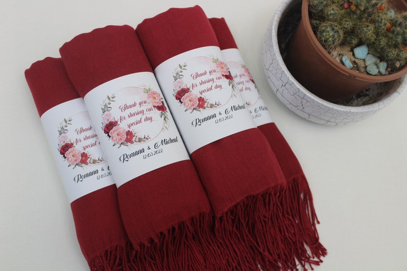 May include: Four burgundy red pashmina scarves with floral and gold accents. Each scarf has a white label with the text "Thank you for sharing our special day" and the names "Romana & Michael" and the date "12.03.2022".