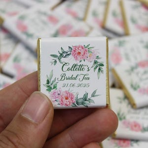 Puede incluir: Una barra de chocolate blanco con un borde dorado y un dise&ntilde;o floral. El texto en la barra de chocolate dice "Collette's Bridal Tea 21.06.2025".