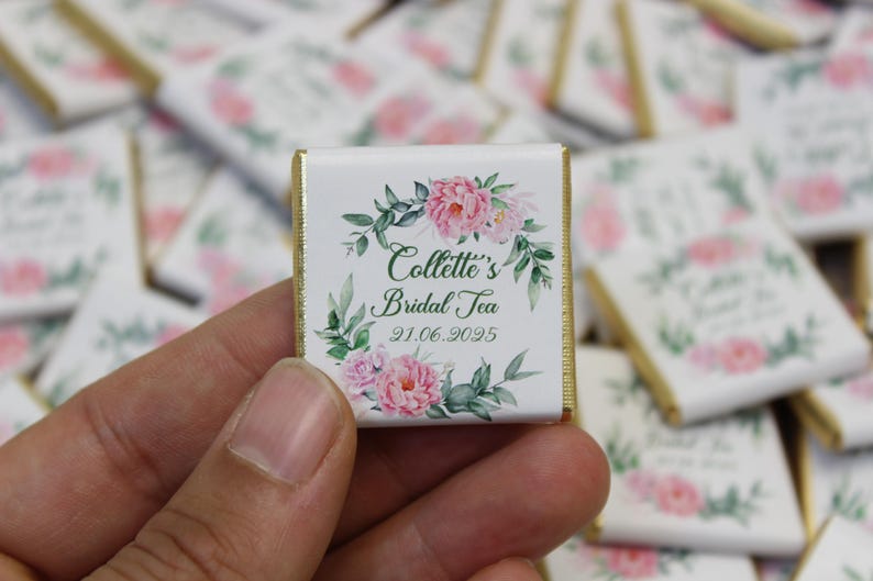 Puede incluir: Una barra de chocolate blanco con un borde dorado y un dise&ntilde;o floral. El texto en la barra de chocolate dice "Collette's Bridal Tea 21.06.2025".