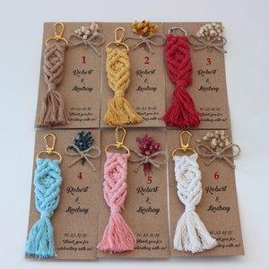 Puede incluir: Seis llaveros con un dise&ntilde;o de macram&eacute; en diferentes colores, incluyendo beige, amarillo, rojo, azul, rosa y blanco. Cada llavero tiene un anillo dorado y una borla. Los llaveros est&aacute;n unidos a peque&ntilde;as tarjetas con el texto "Robert & Lindsay" y la fecha "10.23.2020".