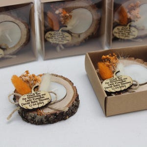 K&ouml;nnte beinhalten: Holz-Teelichthalter mit rustikaler &Auml;sthetik. Jeder Halter hat eine nat&uuml;rliche Holzscheibe mit einer Kerze, Trockenblumen und einem kleinen Holzanh&auml;nger. Der Anh&auml;nger lautet "Thank You For Showering our Little Pumpkin David Baby Shower 13.04.2024".