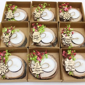 May include: Eight small wooden boxes with lids, each containing a small wooden candle holder with a white candle, a small wooden ornament, and dried flowers. The ornaments have the text "Merry Christmas 2024" or "Happy New Year 2024" on them.