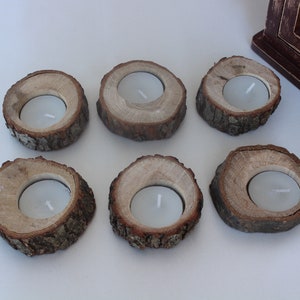 May include: Six rustic wooden candle holders with a natural bark finish. Each holder has a circular opening for a tea light candle.
