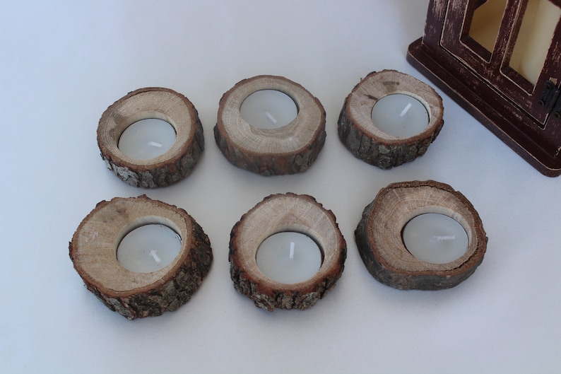 May include: Six rustic wooden candle holders with a natural bark finish. Each holder has a circular opening for a tea light candle.