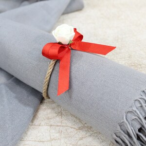 May include: A gray scarf with a red bow and a white flower tied around it.