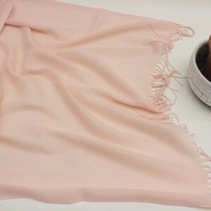 May include: A soft, pale pink scarf with a fringed edge. The scarf is made of a lightweight fabric and is perfect for adding a touch of color to any outfit.