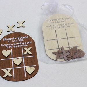 K&ouml;nnte beinhalten: Holz-Tic-Tac-Toe-Spiel-Gastgeschenke. Ein Spiel ist dunkelbraun mit wei&szlig;en Linien und hellfarbigen Herz- und X-Teilen. Das andere ist helles Holz mit braunen X-Teilen. Der Text lautet "Elizabeth & David 21. Juni 2025 Vielen Dank, dass Sie Teil unseres besonderen Tages waren."