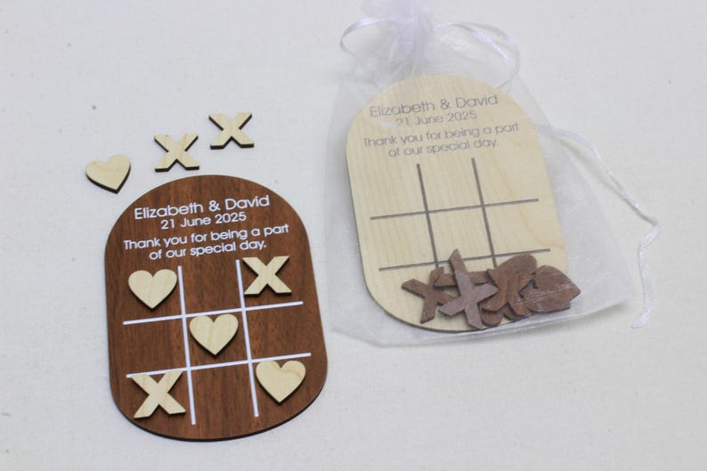 K&ouml;nnte beinhalten: Holz-Tic-Tac-Toe-Spiel-Gastgeschenke. Ein Spiel ist dunkelbraun mit wei&szlig;en Linien und hellfarbigen Herz- und X-Teilen. Das andere ist helles Holz mit braunen X-Teilen. Der Text lautet "Elizabeth & David 21. Juni 2025 Vielen Dank, dass Sie Teil unseres besonderen Tages waren."