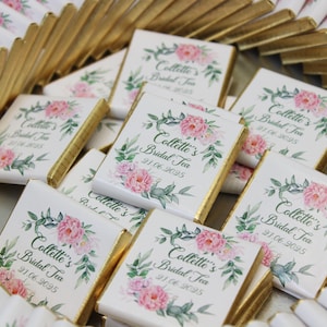 Puede incluir: Una colecci&oacute;n de barras de chocolate blanco envueltas en papel de oro con dise&ntilde;os florales y el texto "Collette's Bridal Tea" y una fecha.