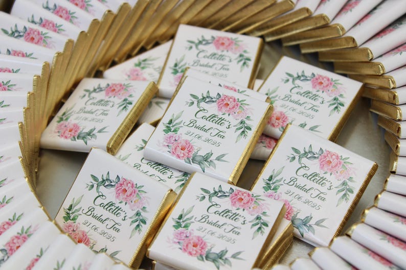 Puede incluir: Una colecci&oacute;n de barras de chocolate blanco envueltas en papel de oro con dise&ntilde;os florales y el texto "Collette's Bridal Tea" y una fecha.