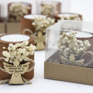 May include: A set of small wooden candle holders with dried white flowers and a wooden angel cutout. The angel cutout has the text "Rosalyn, you will always be in our hearts!"