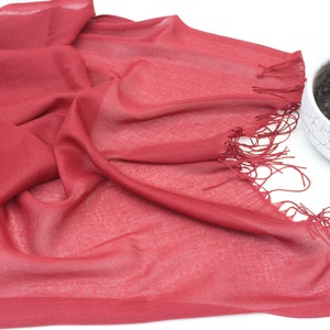 May include: A soft, red scarf with a fringed edge. The scarf is made of a lightweight fabric and is perfect for adding a touch of colour to any outfit.