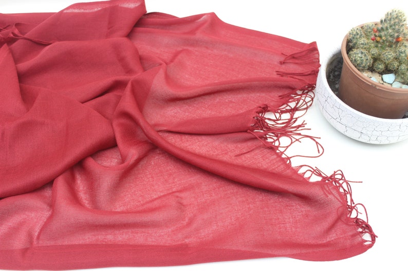 May include: A soft, red scarf with a fringed edge. The scarf is made of a lightweight fabric and is perfect for adding a touch of colour to any outfit.