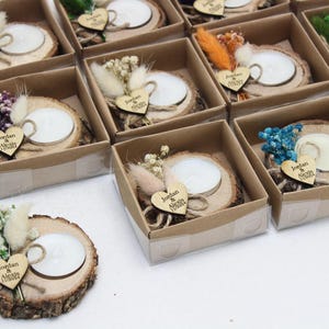 May include: A collection of small, decorative candle holders. Each candle sits on a wooden slice and is adorned with dried flowers and a wooden heart with text. The candle holders are packaged in small, clear boxes.