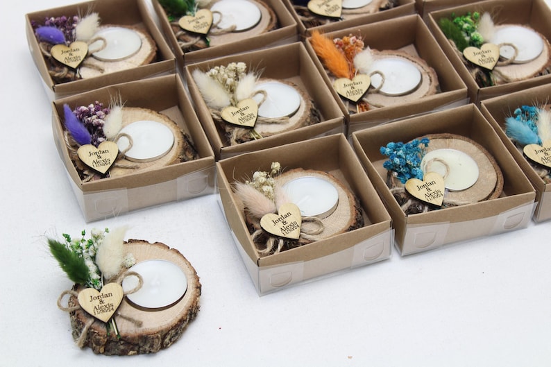 May include: A collection of small, decorative candle holders. Each candle sits on a wooden slice and is adorned with dried flowers and a wooden heart with text. The candle holders are packaged in small, clear boxes.