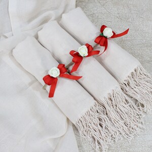 May include: Three white pashmina scarves with red ribbon bows and white flower accents. The scarves are folded and stacked on top of each other.
